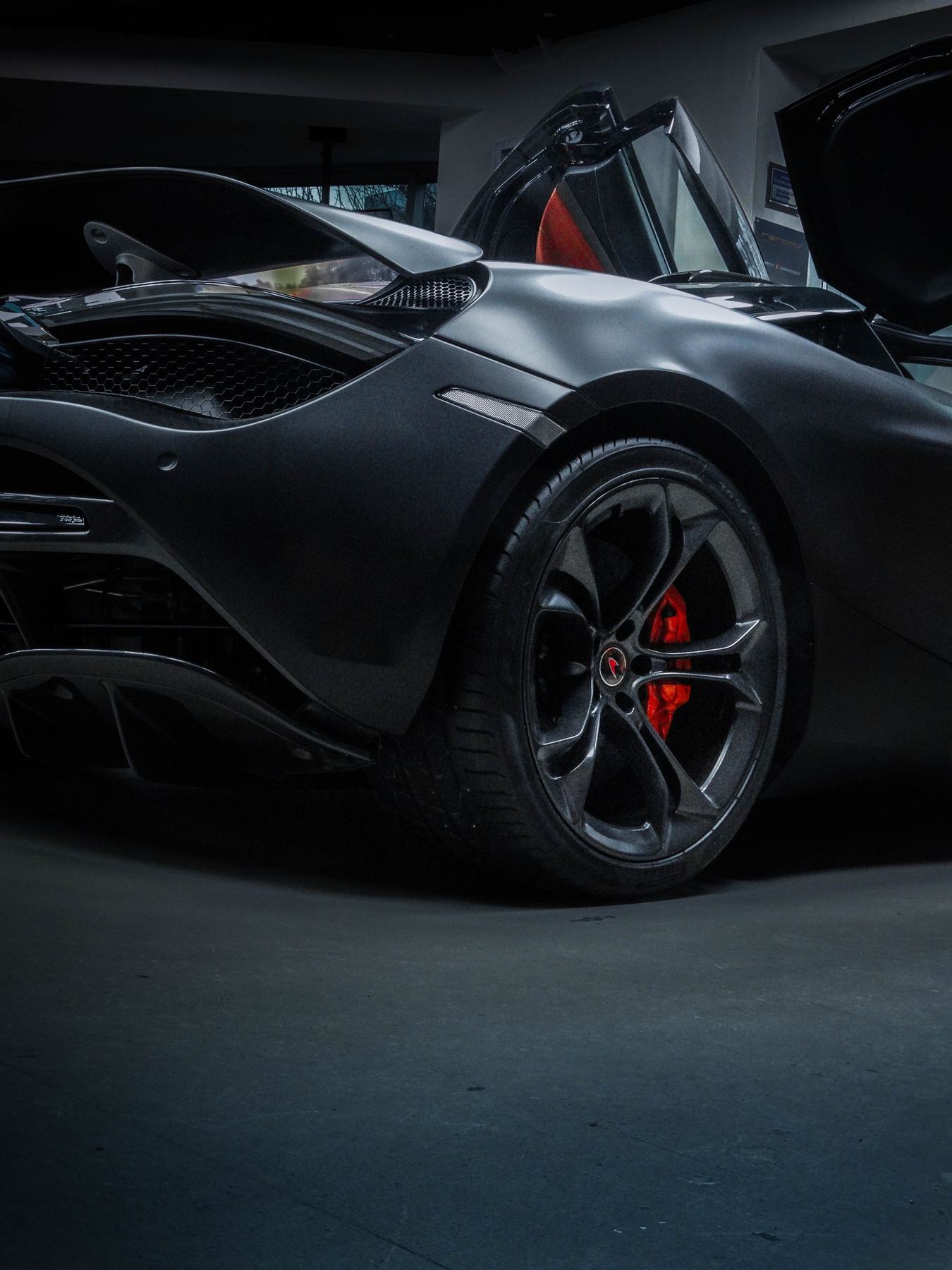 Matte black McLaren 720S with its doors open in a dark garage